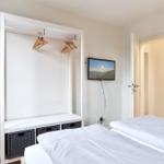 Zwei Betten, Kleiderschrank mit Haken und Fernseher an der Wand.