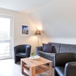 Wohnzimmer mit Sofa, zwei Sesseln, Couchtisch und TV. Fenster zum Balkon.