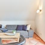 Wohnzimmer mit Sofa, Sessel und Holztisch. Terrakottafußboden und schräge Decke.