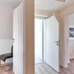 Flur mit Türen und Stuhl. Holzgeländer und Wandbild sichtbar.