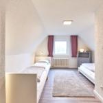 Zimmer mit zwei Betten, Fenster, Heizung und Teppichboden.