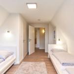 Zwei Einzelbetten in einem Dachgeschosszimmer mit Holzboden und Stehlampe.