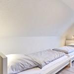 Zwei Betten in einem Schlafzimmer mit Dachschräge und Fenster mit Vorhang.