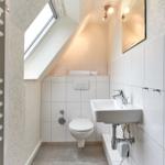 Badezimmer mit Toilette, Waschbecken und Dusche unter Dachschräge mit Fenster.
