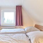 Schlafzimmer mit Doppelbett, Fenster und rosa Vorhängen.