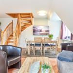 Wohn- und Essbereich mit Holztreppe, Sofa, Sessel und Esstisch.