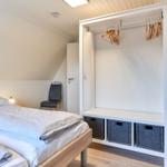 Schlafzimmer mit Bett, Kleiderschrank und Stuhl unter schrägen Dachdecken.