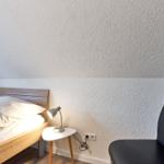 Schlafzimmer mit Bett, Nachttisch und Stuhl. Wand mit strukturiertem Putz.