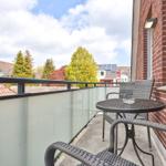 Terrasse mit Tisch und Stühlen, Glasgeländer und Blick auf Bäume und Dächer.