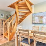 Esszimmer mit Holztisch, Stühlen und spiralförmiger Treppe. Fernseher zeigt Strandbild.