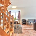 Eingangsbereich mit Holztreppe, Essbereich und Wohnzimmer mit Sofa und Sesseln.