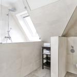 Dusche mit Dachfenster, Toilette und Handtuchständer in hellen Fliesen.