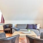 Wohnzimmer mit Sofa, zwei Ledersesseln und Holztisch unter schrägem Dach.