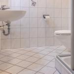 Badezimmer mit Waschbecken, Toilette und Dusche. Fliesenwand und Boden.