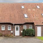 Ein Haus mit rotem Ziegeldach, weißen Türen und Fenstern sowie einem gepflasterten Vorplatz.
