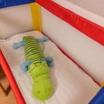 Ein Kinderbett mit einem grünen Krokodil-Stofftier und einem weißen Laken.