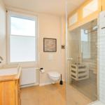 Badezimmer mit Dusche, Waschbecken und Toilette. Holzfußboden und Fenster mit Jalousie.