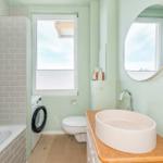 Badezimmer mit Badewanne, Waschmaschine und Waschtisch mit runden Spiegel.