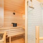 Sauna mit Holzbänken und Dusche mit Fliesenwand.