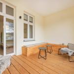 Terrasse mit Holzboden, Sitzbank, zwei Stühlen und Tischen. Durchgang ins Innere.