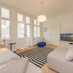Wohnzimmer mit Sofa, Fernseher und großen Fenstern.