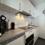 Küche mit Arbeitsfläche, Spüle, Herd und Backofen. An der Wand hängt eine Uhr.