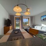 Wohn- und Essbereich mit Sofa, Esstisch und TV. Fenster und Tür zur Außenterrasse.