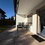Terrasse mit Tisch und Stühlen, Tür zum Innenraum, Blick auf Garten und Nachbarhaus.