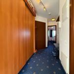 Flur mit Holzwand, blauem Teppich und Blick in Schlafzimmer.