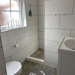 Badezimmer mit Toilette, Waschbecken und Dusche. Bodenfliesen und Wandfliesen sind weiß.