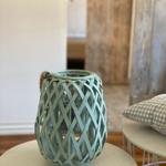 Ein mintfarbener, geflochtener Leuchter steht auf einem runden Tisch.