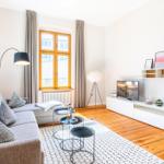 Wohnzimmer mit Sofa, TV und Holzboden. Fenster mit Vorhängen und Beleuchtung.