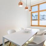 Esszimmer mit weißem Tisch, weißen Stühlen und drei kupferfarbenen Hängelampen an der Wand.