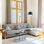 Ein Wohnzimmer mit Sofa, zwei Tischen und Fenstern mit Vorhängen.