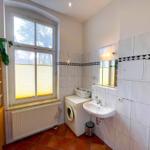 Badezimmer mit Waschmaschine, Waschbecken und Fenster mit Jalousie.