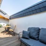Terrasse mit Sitzgelegenheit, Tisch, Stühlen und Pflanzen unter Dach