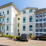 Fünfgeschossiges Gebäude mit Balkonen und Fenstern. Zwei Autos parken vor dem Haus.