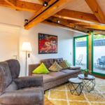 Wohnzimmer mit Sofa, Sessel und Glasfront zur Terrasse.