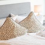 Doppelbett mit Kissen und Nachttisch. Lampe und grüner Rahmen sichtbar.