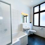 Badezimmer mit Badewanne, Dusche, Waschbecken und Toilette. Große Fenster mit Milchglas.