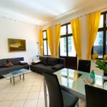 Wohn- und Essbereich mit zwei Sofas, Glas-Tisch und gelben Vorhängen.