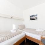 Zwei Einzelbetten mit karierten Bettwäsche, Wandbild und Nachttisch mit Wecker.