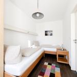 Zwei Einzelbetten mit Kissen und Bettwäsche. Holzfußboden, Deckenventilator und Wandbild.