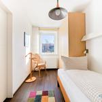 Ein Schlafzimmer mit Bett, Kleiderschrank und Stuhl vor dem Fenster.