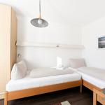 Zwei Einzelbetten mit karierten Bezügen und weißen Matratzen. Holzmöbel und Wandbild.