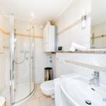 Badezimmer mit Dusche, Waschbecken und Toilette. Fliesen und Spiegel sichtbar.