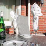 Tisch mit Flasche Secco, zwei Gläsern und Tellern auf Terrasse mit Backsteinwand.