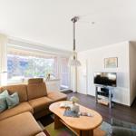 Wohnzimmer mit Sofa, Couchtisch und Fernseher. Fenster mit Blick auf Balkon.