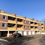 Rotes Backsteinhaus mit Balkonen und Garagen. Ein Auto steht auf dem Hof.