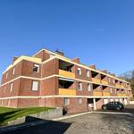 Rotes Backsteingebäude mit Balkonen und Parkplatz vor einem klaren Himmel.